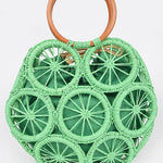 Palm-green raffia woven sunburst circle handbag with wooden ring handles—boho straw tote for vacation.