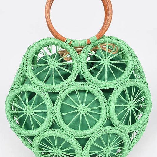 Palm-green raffia woven sunburst circle handbag with wooden ring handles—boho straw tote for vacation.