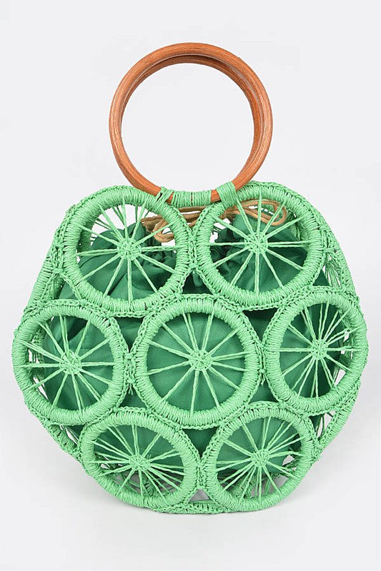 Palm-green raffia woven sunburst circle handbag with wooden ring handles—boho straw tote for vacation.