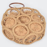 Natural raffia woven circle handbag with wooden ring handles and sunburst pattern—neutral beach tote
