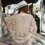 Woman wearing a beige crochet tie-front kimono over a white top and checkered mini skirt, accessorized with a hat and bracelets.