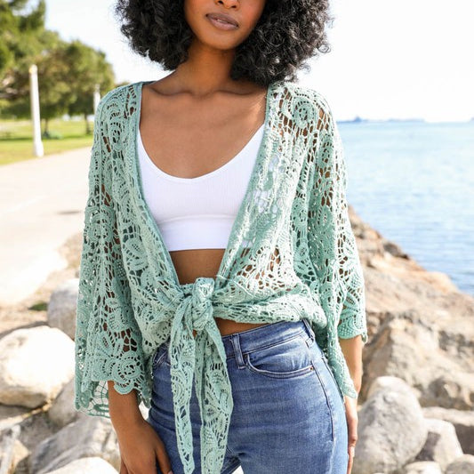 Close-up of mint green floral crochet wrap tied at the front, worn over a white crop top.