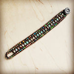 Handmade leather wrap bracelet with colorful semi-precious stone beads and a silver floral button clasp, laid out on a light wooden surface.