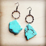 Chunky blue turquoise dangle earrings with hammered metal hoops, featuring large natural stones on a light wooden background.