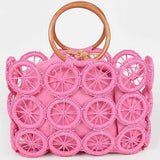 Bright pink woven circle-grid raffia tote with wooden ring handles and removable drawstring pouch.