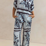 Light blue floral two-piece lounge set for women with short-sleeve button-down shirt and drawstring wide-leg pants, featuring navy botanical print – perfect for vacation, resort wear, or chic loungewear looks.