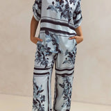 Light blue floral two-piece lounge set for women with short-sleeve button-down shirt and drawstring wide-leg pants, featuring navy botanical print – perfect for vacation, resort wear, or chic loungewear looks.