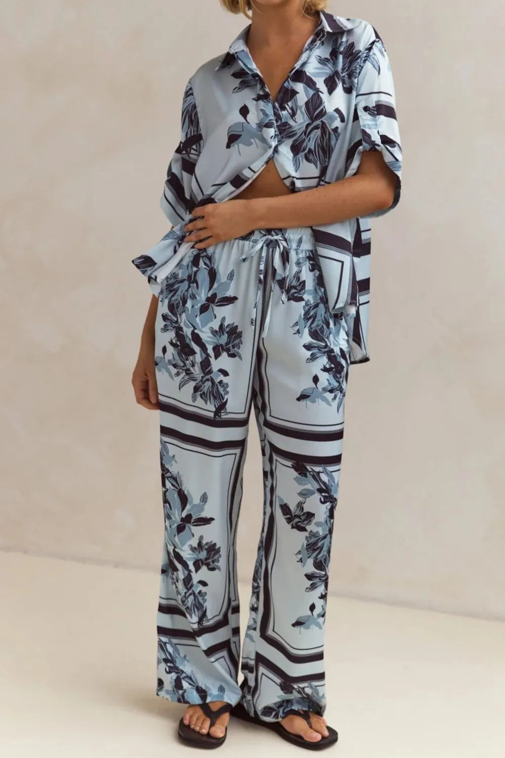 Light blue floral two-piece lounge set for women with short-sleeve button-down shirt and drawstring wide-leg pants, featuring navy botanical print – perfect for vacation, resort wear, or chic loungewear looks.