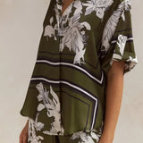 Olive green floral lounge set for women featuring short-sleeve button-down top and wide-leg pants with white botanical print – perfect for casual chic or resort wear.