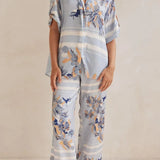 Model wearing a light blue floral lounge set with short-sleeve button-down top and wide-leg pants, featuring peach, navy, and white accents.