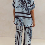 Light blue floral two-piece lounge set for women with short-sleeve button-down shirt and drawstring wide-leg pants, featuring navy botanical print – perfect for vacation, resort wear, or chic loungewear looks.