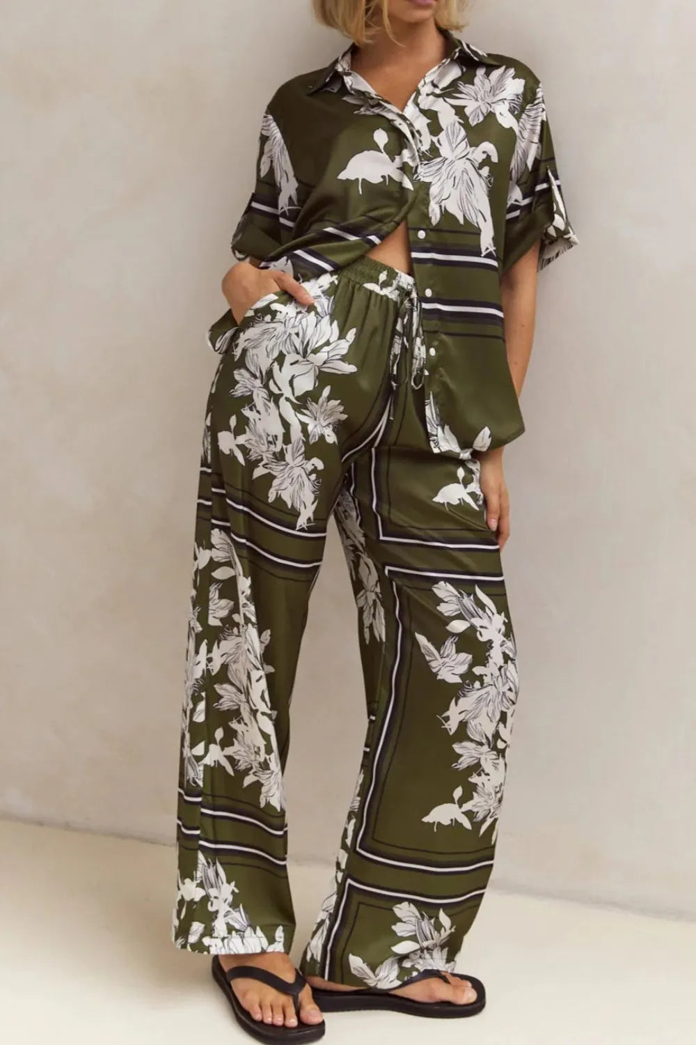 Olive green floral lounge set for women featuring short-sleeve button-down top and wide-leg pants with white botanical print – perfect for casual chic or resort wear.