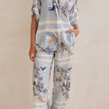 Model wearing a light blue floral lounge set with short-sleeve button-down top and wide-leg pants, featuring peach, navy, and white accents.