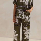 Olive green floral lounge set for women featuring short-sleeve button-down top and wide-leg pants with white botanical print – perfect for casual chic or resort wear.