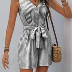 Woman wearing a black and white vertical striped belted romper with front buttons and tie waist, holding a straw bag.
