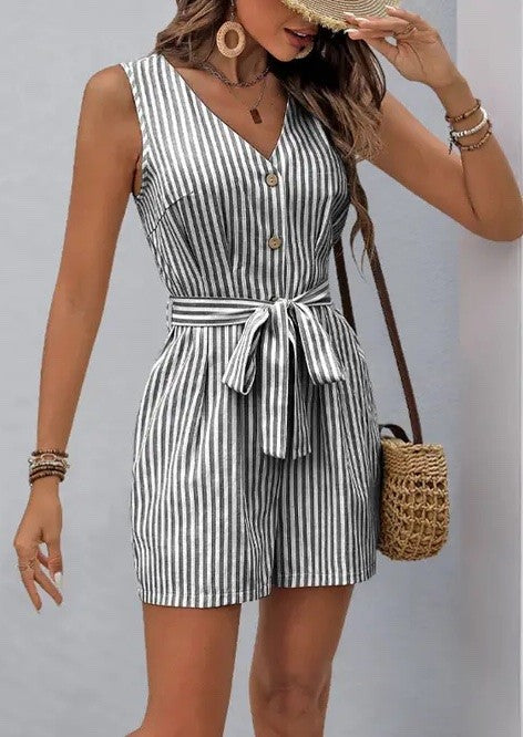 Woman wearing a black and white vertical striped belted romper with front buttons and tie waist, holding a straw bag.