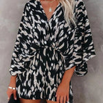 Women's black and taupe abstract animal-print kimono-sleeve romper with deep V-neck, cinched elastic waist, and flowy shorts.
