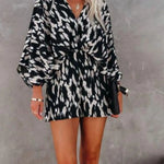 Women's black and taupe abstract animal-print kimono-sleeve romper with deep V-neck, cinched elastic waist, and flowy shorts.