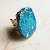 Large blue regalite stone statement ring with hammered adjustable metal band, displayed on a light wooden background.