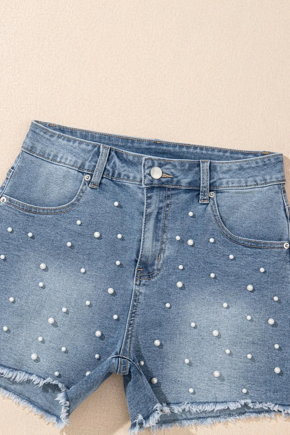 Women's high-waisted denim shorts with faux pearl embellishments and frayed hem – trendy summer jean shorts for casual and chic outfits.