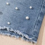 Women's high-waisted denim shorts with faux pearl embellishments and frayed hem – trendy summer jean shorts for casual and chic outfits. Showing the detail.