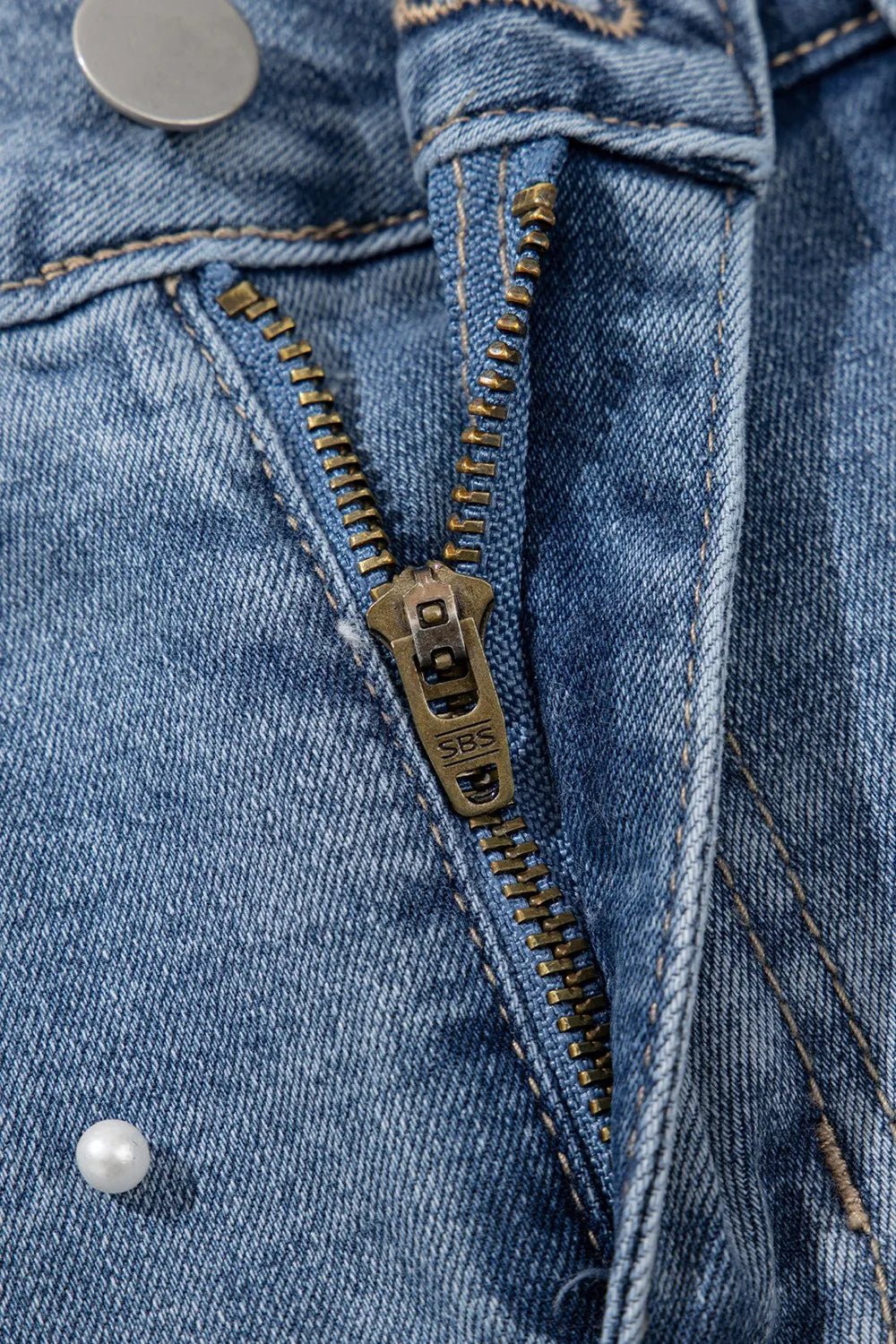 Women's high-waisted denim shorts with faux pearl embellishments and frayed hem – trendy summer jean shorts for casual and chic outfits. Showing the detail.