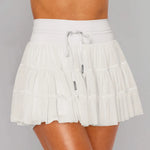 Women's white tiered ruffle sport skort featuring high-rise drawstring waist and integrated compression shorts for tennis or running.