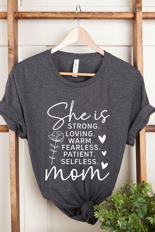 Dark Grey graphic T-shirt reading ‘She is strong, loving, warm, fearless, patient, selfless—mom’ styled flat-lay with tan fedora, denim shorts, and greenery.