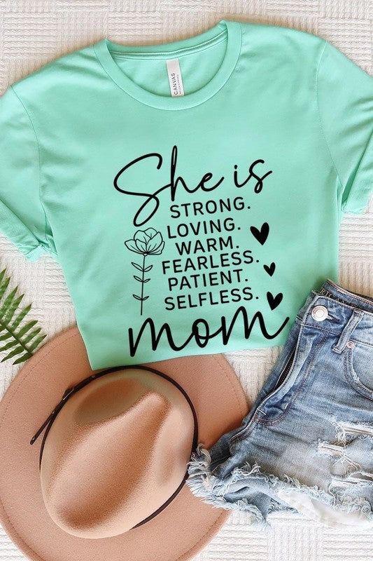 Light Green graphic T-shirt reading ‘She is strong, loving, warm, fearless, patient, selfless—mom’ styled flat-lay with tan fedora, denim shorts, and greenery.