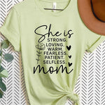 Light Green graphic T-shirt reading ‘She is strong, loving, warm, fearless, patient, selfless—mom’ styled flat-lay with tan fedora, denim shorts, and greenery.