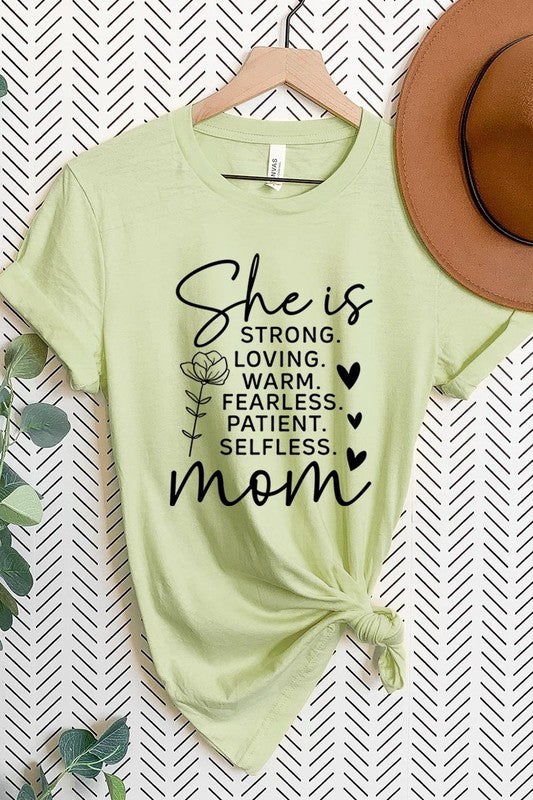 Light Green graphic T-shirt reading ‘She is strong, loving, warm, fearless, patient, selfless—mom’ styled flat-lay with tan fedora, denim shorts, and greenery.