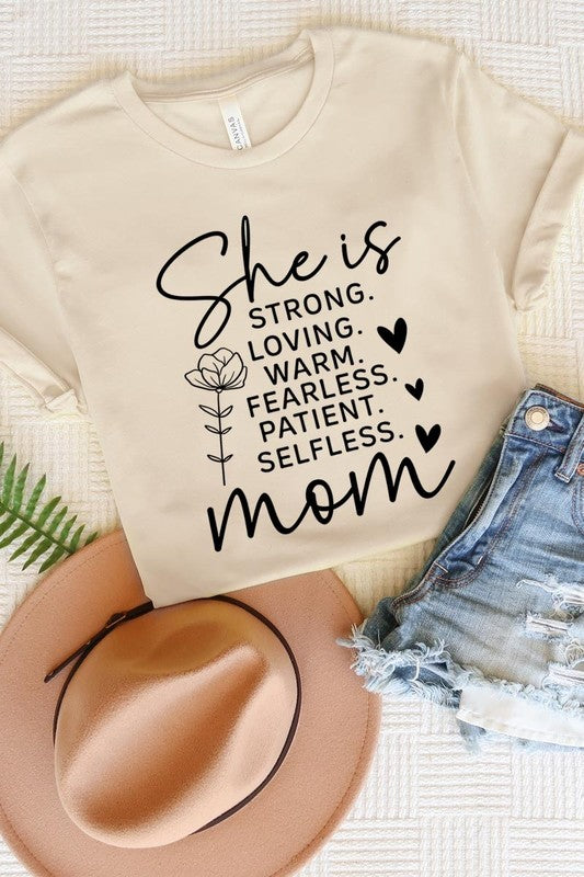 Off White graphic T-shirt reading ‘She is strong, loving, warm, fearless, patient, selfless—mom’ styled flat-lay with tan fedora, denim shorts, and greenery.