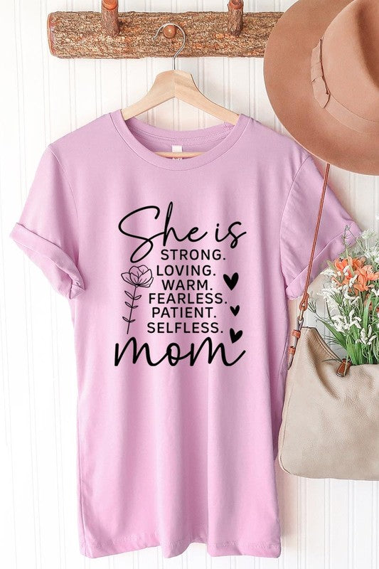 Pink graphic T-shirt reading ‘She is strong, loving, warm, fearless, patient, selfless—mom’ styled flat-lay with tan fedora, denim shorts, and greenery.