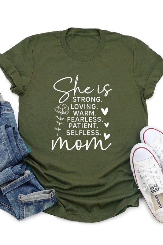 Army green graphic T-shirt reading ‘She is strong, loving, warm, fearless, patient, selfless—mom’ styled flat-lay with tan fedora, denim shorts, and greenery.