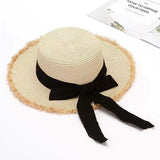 Cream straw sun hat with frayed brim and long grosgrain bow ribbon tied at the back, displayed against a soft floral backdrop.