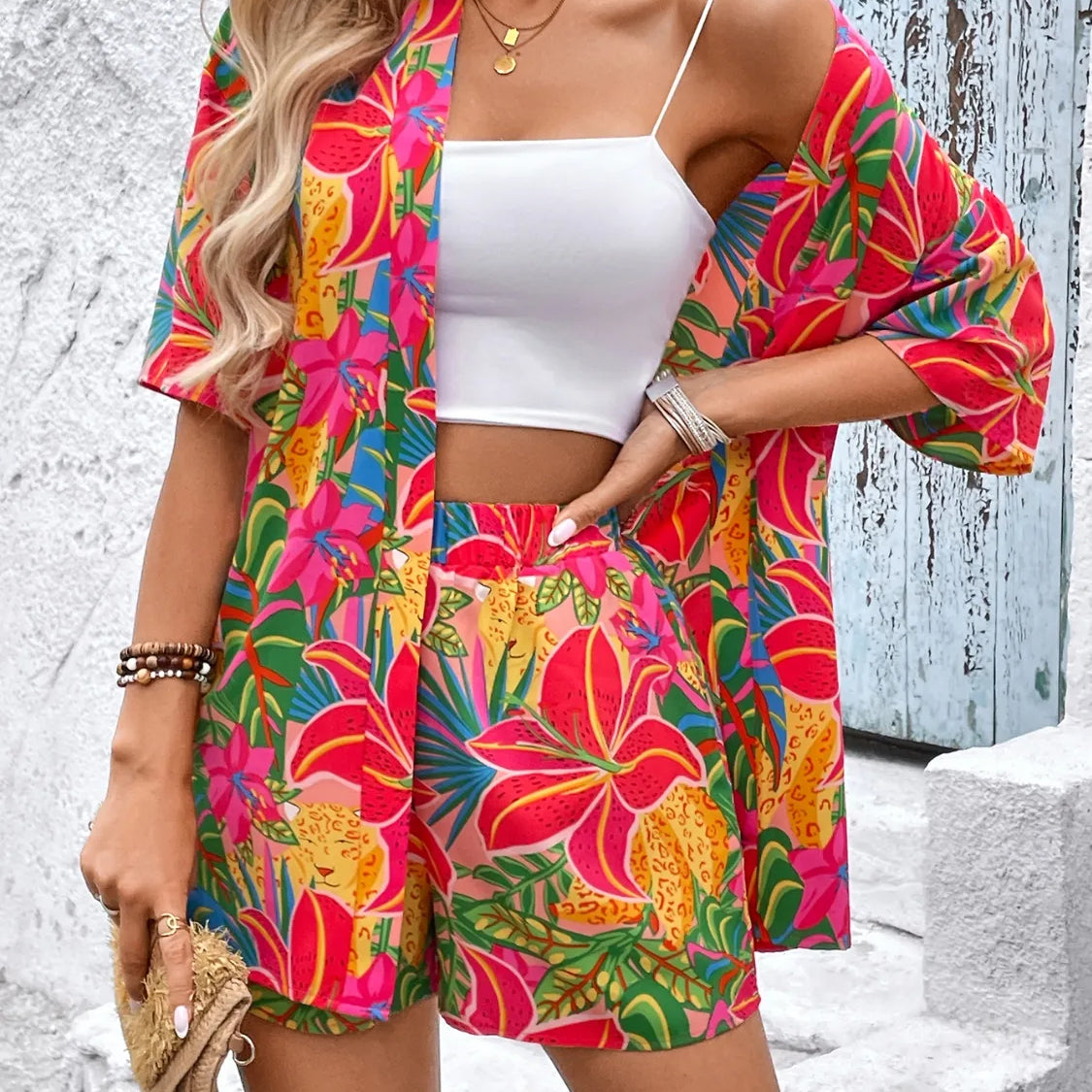 Women's tropical floral two-piece set with relaxed short-sleeve button shirt and high-waist shorts in vibrant fuchsia, coral, lime, and turquoise hibiscus print – lightweight resort outfit.