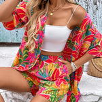 Women's tropical floral two-piece set with relaxed short-sleeve button shirt and high-waist shorts in vibrant fuchsia, coral, lime, and turquoise hibiscus print – lightweight resort outfit.