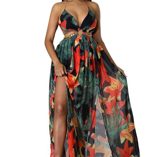 Woman wearing a vibrant tropical floral cut-out halter maxi dress with gold chain belt and thigh-high slit.