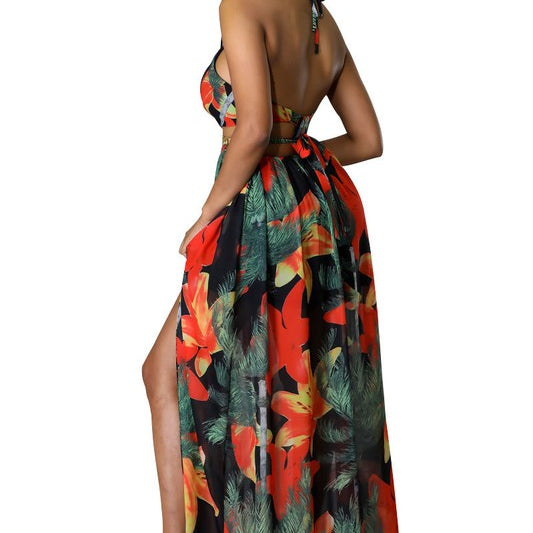 Woman wearing a vibrant tropical floral cut-out halter maxi dress with gold chain belt and thigh-high slit.