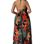 Woman wearing a vibrant tropical floral cut-out halter maxi dress with gold chain belt and thigh-high slit.