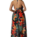Woman wearing a vibrant tropical floral cut-out halter maxi dress with gold chain belt and thigh-high slit.