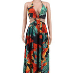 Woman wearing a vibrant tropical floral cut-out halter maxi dress with gold chain belt and thigh-high slit.