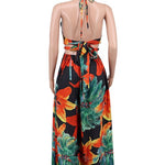 Woman wearing a vibrant tropical floral cut-out halter maxi dress with gold chain belt and thigh-high slit.
