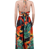Woman wearing a vibrant tropical floral cut-out halter maxi dress with gold chain belt and thigh-high slit.