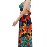 Woman wearing a vibrant tropical floral cut-out halter maxi dress with gold chain belt and thigh-high slit.