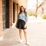 Woman styling a black high-waisted tummy-control skort with built-in shorts and flared A-line overlay, showcasing slimming athletic fit for tennis, golf or everyday wear.