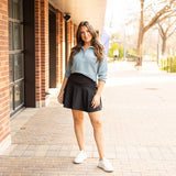 Woman styling a black high-waisted tummy-control skort with built-in shorts and flared A-line overlay, showcasing slimming athletic fit for tennis, golf or everyday wear.