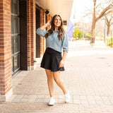 Woman styling a black high-waisted tummy-control skort with built-in shorts and flared A-line overlay, showcasing slimming athletic fit for tennis, golf or everyday wear.