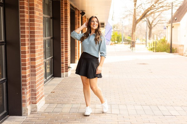 Woman styling a black high-waisted tummy-control skort with built-in shorts and flared A-line overlay, showcasing slimming athletic fit for tennis, golf or everyday wear.