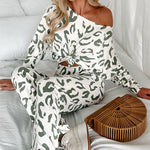 Woman lounging in bed wearing a sage leopard print lounge set with an off-shoulder knotted top and white sneakers.